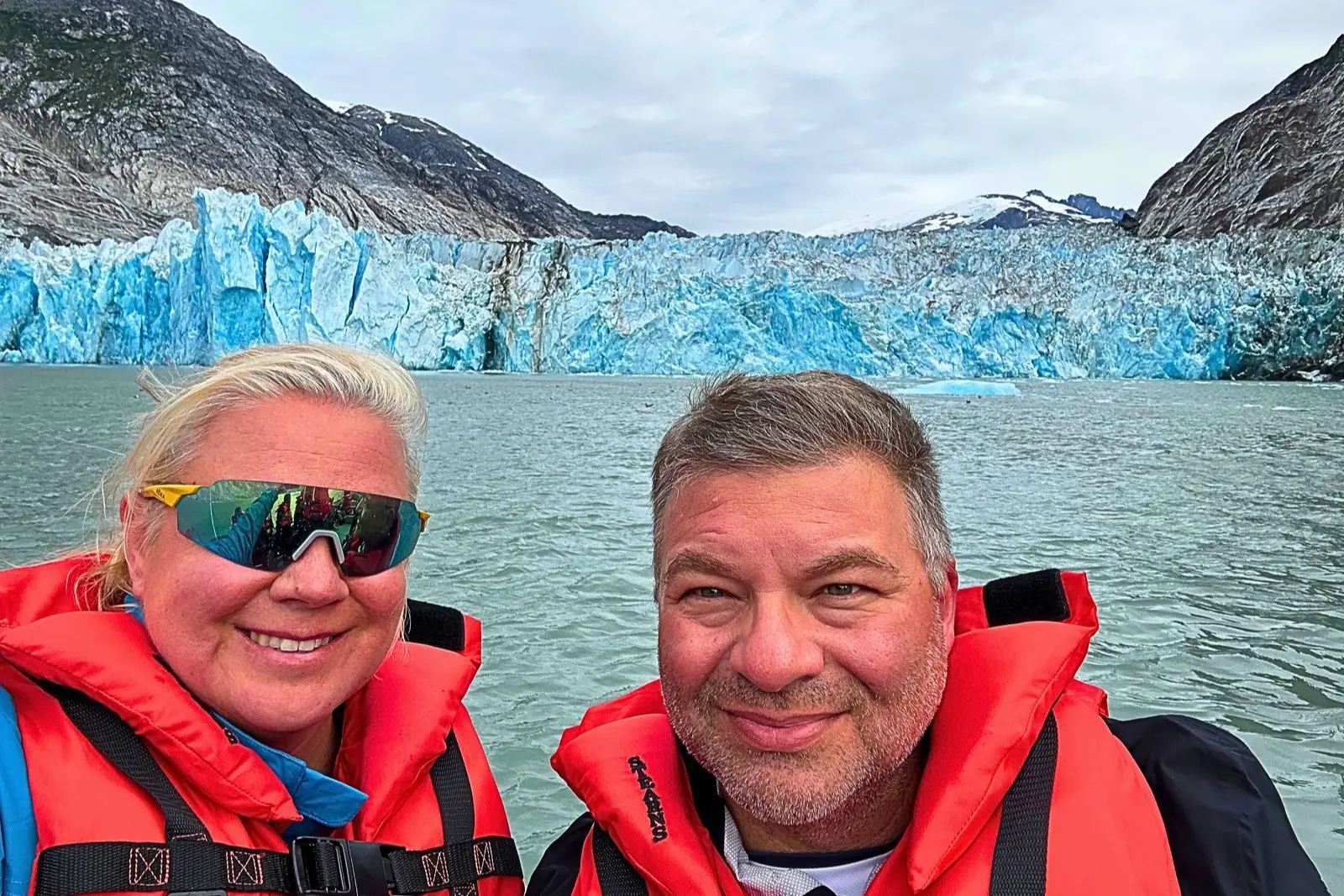 A selfie of Erika and Chris Commisso in a Zodiac, with the blue face of Dawes Glacier behind them.