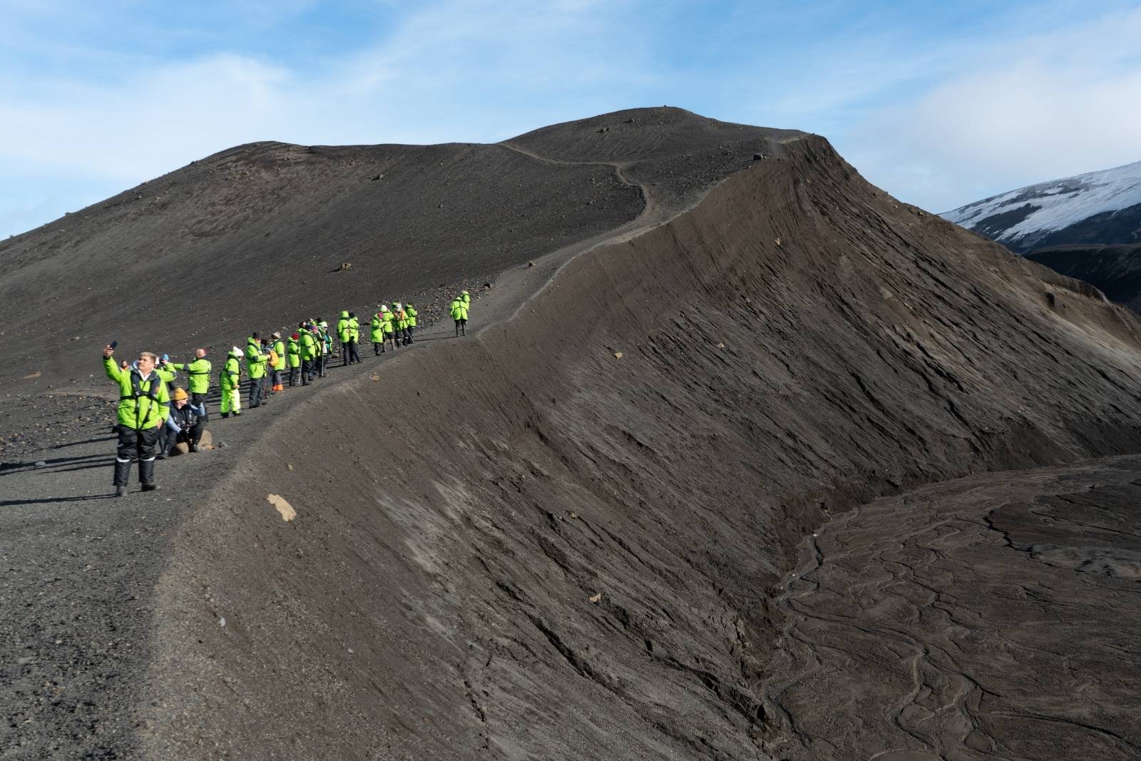 Expedition travelers hiking along a dark volcanic ridge on Deception Island.