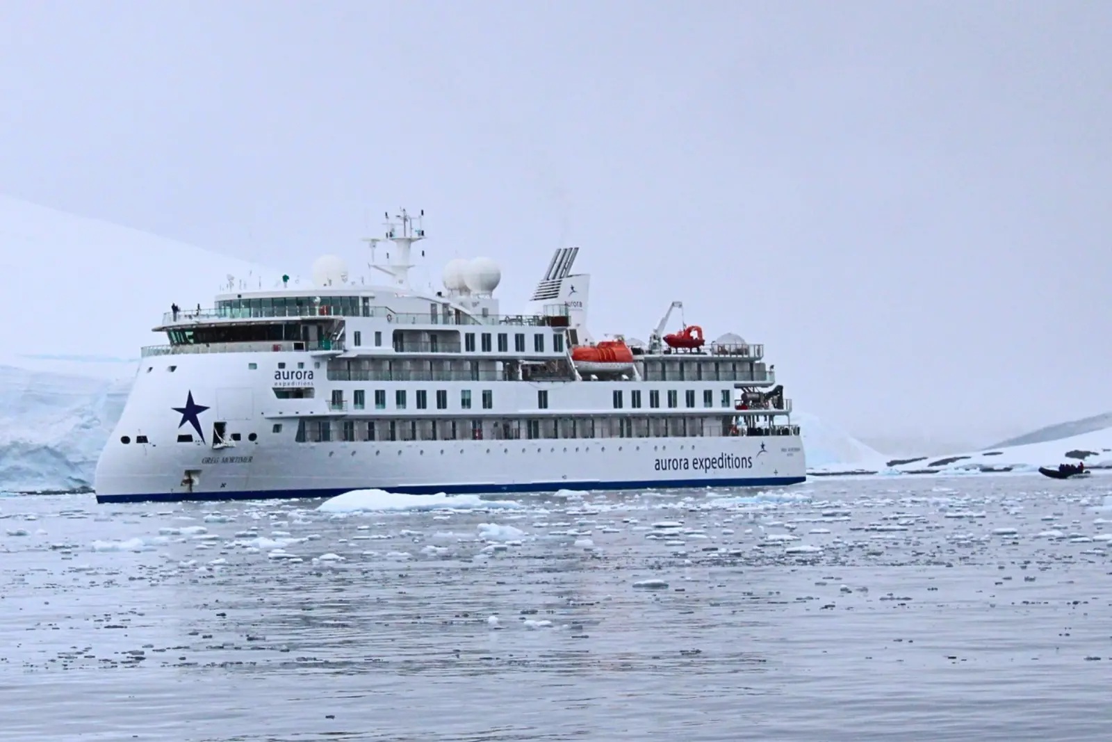 The Greg Mortimer in a bay filled with brash ice, with a Zodiac heading out beside her and a glacier behind.