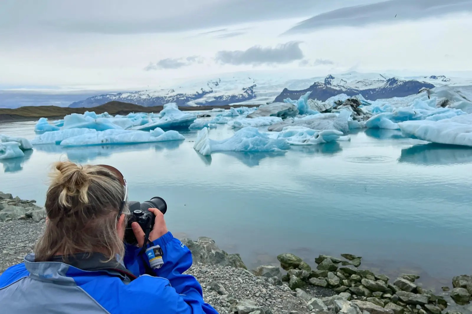 Erika Commisso photographing icebergs in Jökulsárlón glacier lagoon, with a glacier and mountains behind.