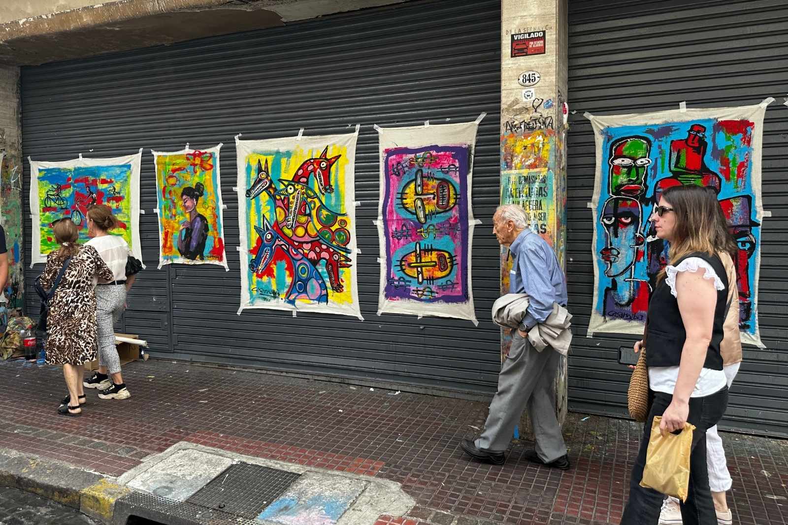 Pedestrians passing colorful paintings displayed at the Feria de San Telmo in Buenos Aires.