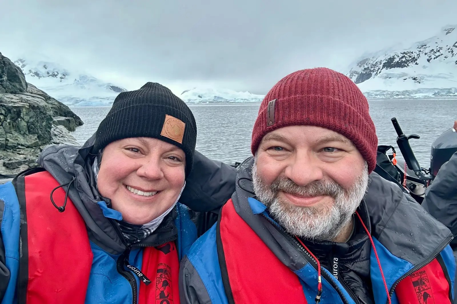 Erika and Chris Commisso in Aurora life jackets in a Zodiac, with snow-covered mountains behind them.