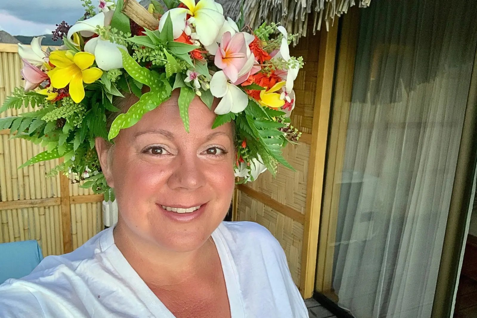 Erika Commisso wearing a large Hei flower crown of plumeria, lilies and ferns on a bungalow deck.