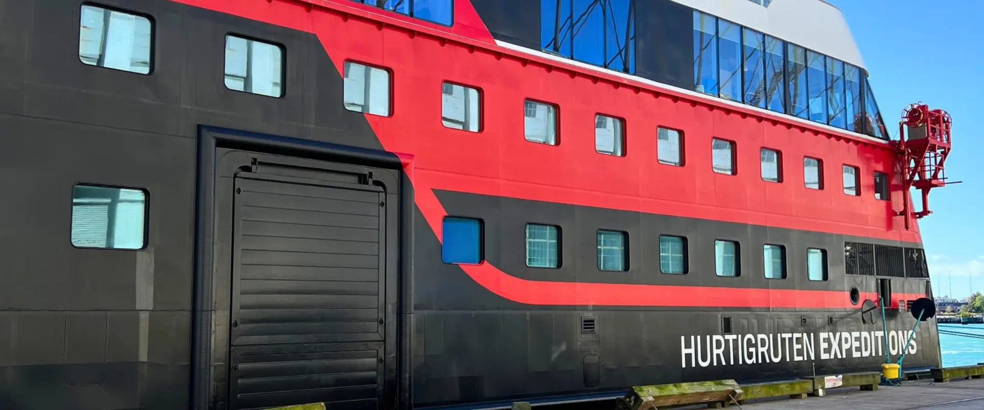 The black and red hull of the Roald Amundsen alongside the pier in Boston, painted 'Hurtigruten Expeditions'.