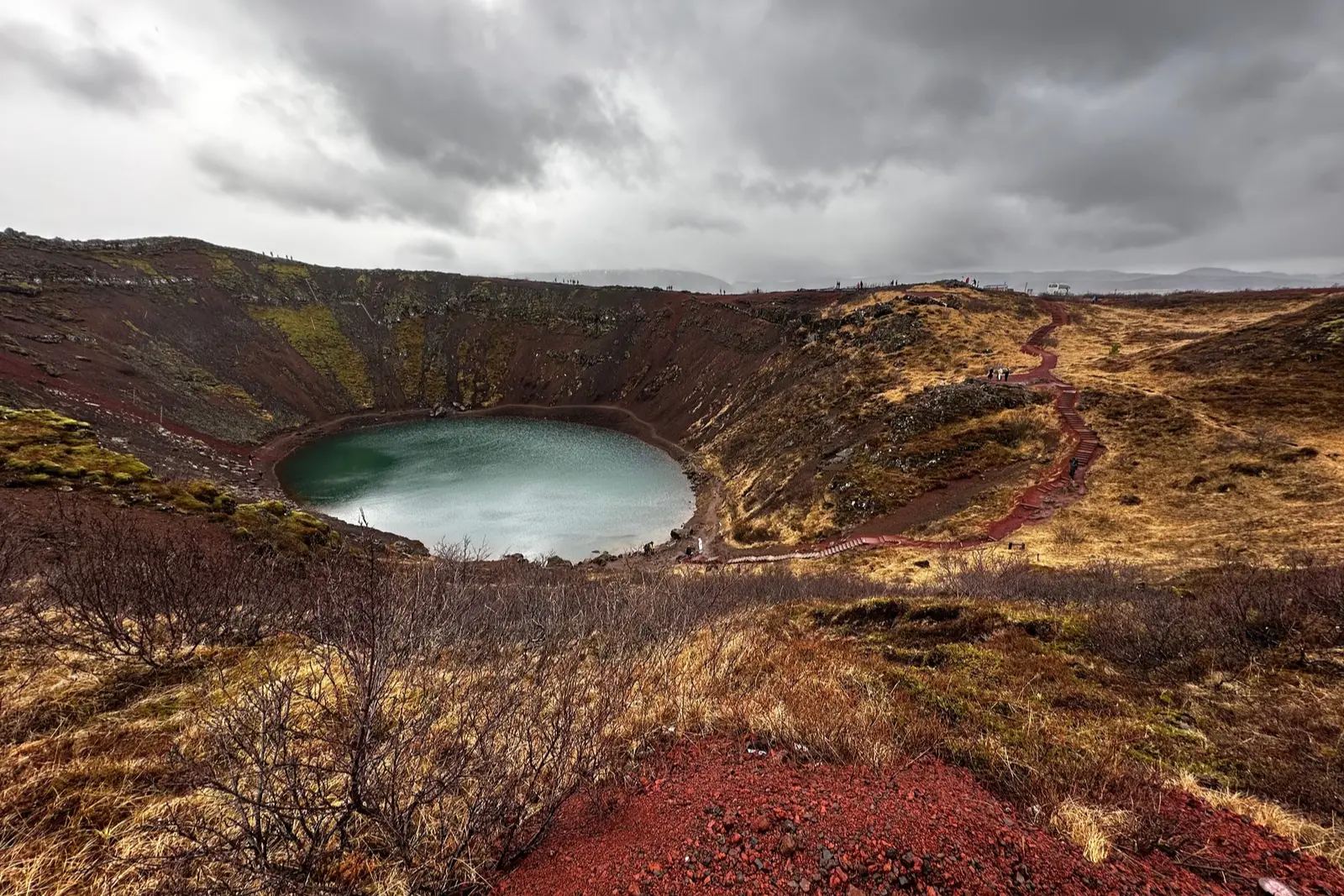 Kerið crater, with a turquoise lake below red and gold slopes and a red-stepped path down to the water.