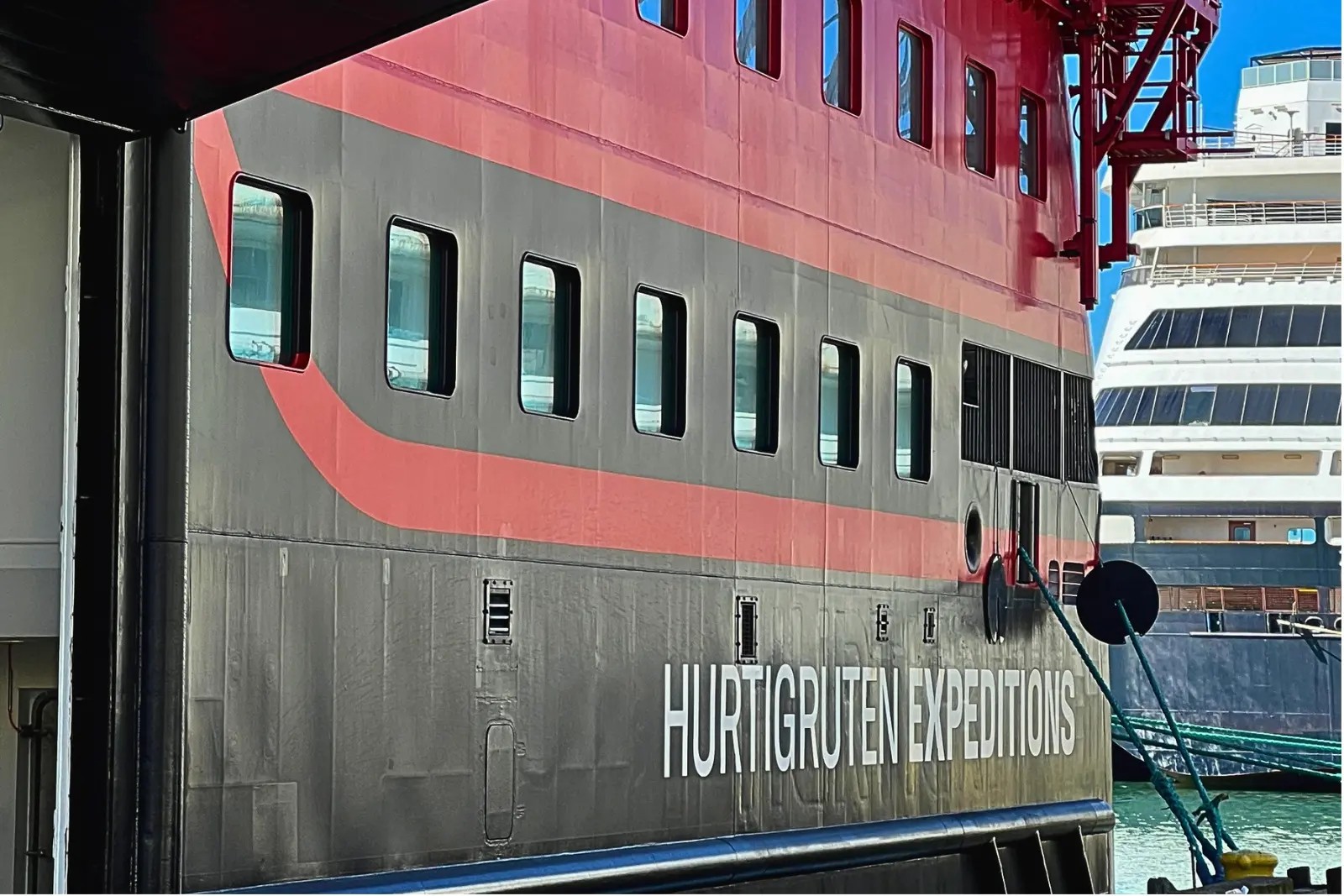 Close-up of the Roald Amundsen's black and red hull reading 'Hurtigruten Expeditions', with another cruise ship berthed behind.