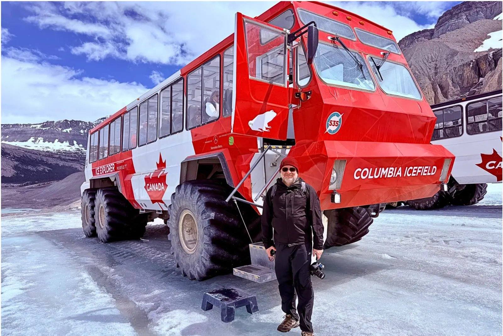 Chris Commisso standing by a red Ice Explorer bus on the Athabasca Glacier at the Columbia Icefield.