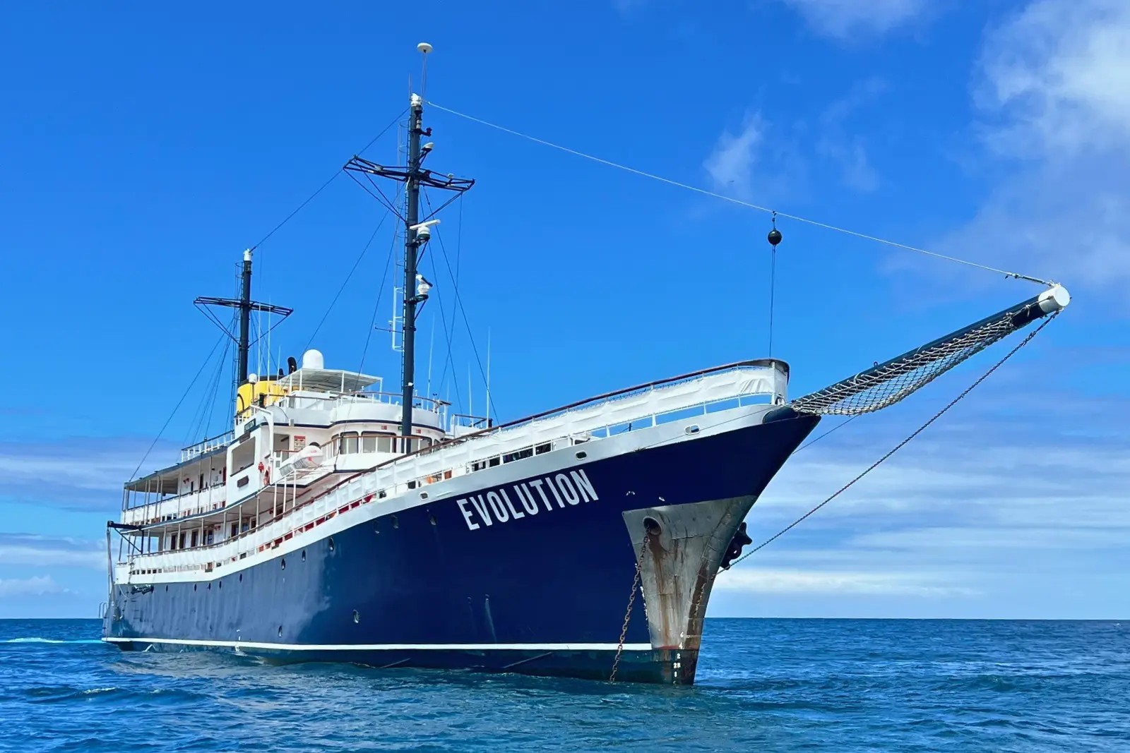 The Evolution at anchor, seen close from a panga, with her bow netting and dark blue hull.