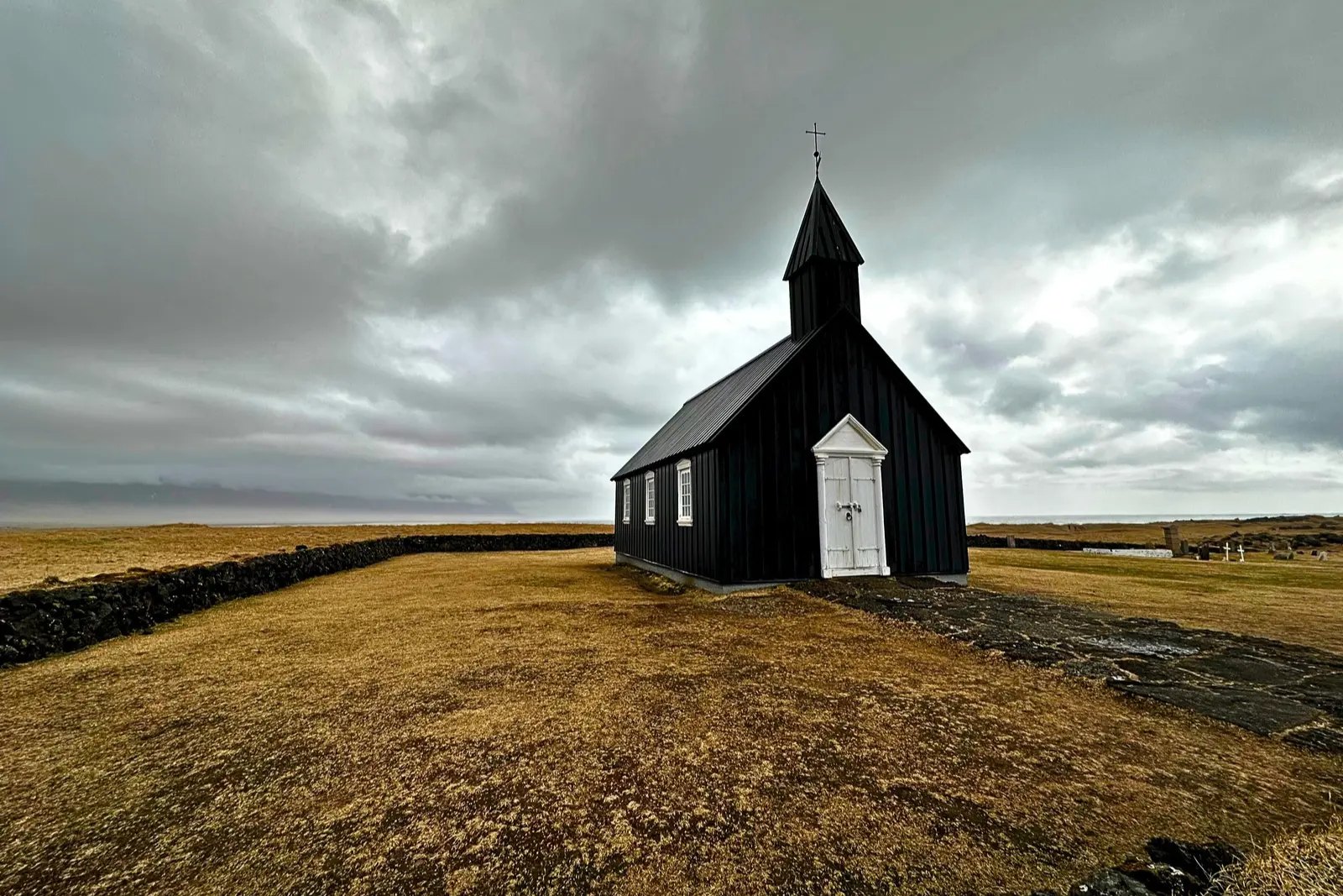 Búðakirkja, a black wooden church with white doors, on brown grass under a stormy sky.