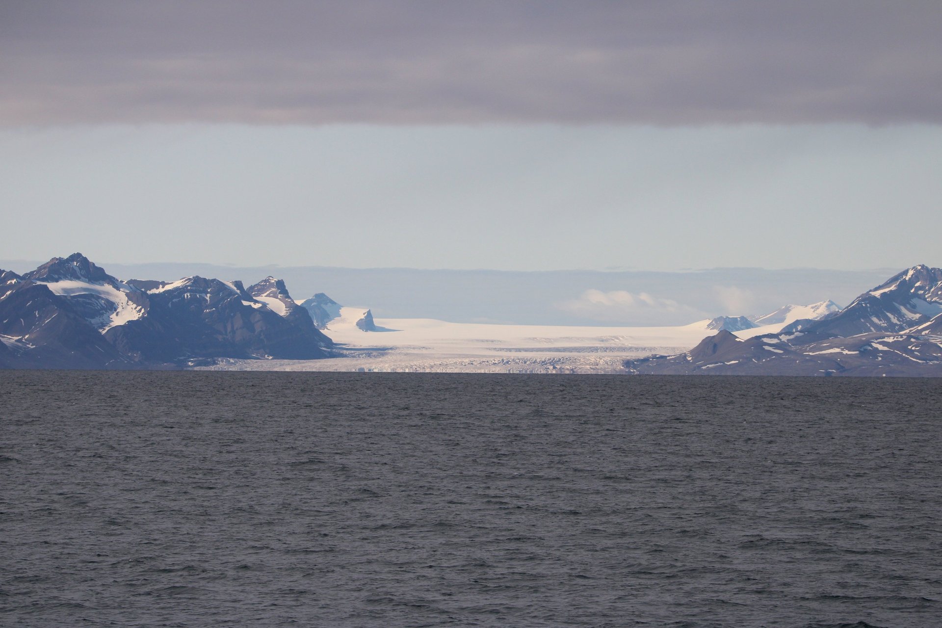 A glacier flowing between mountains to the sea on a remote polar coastline.