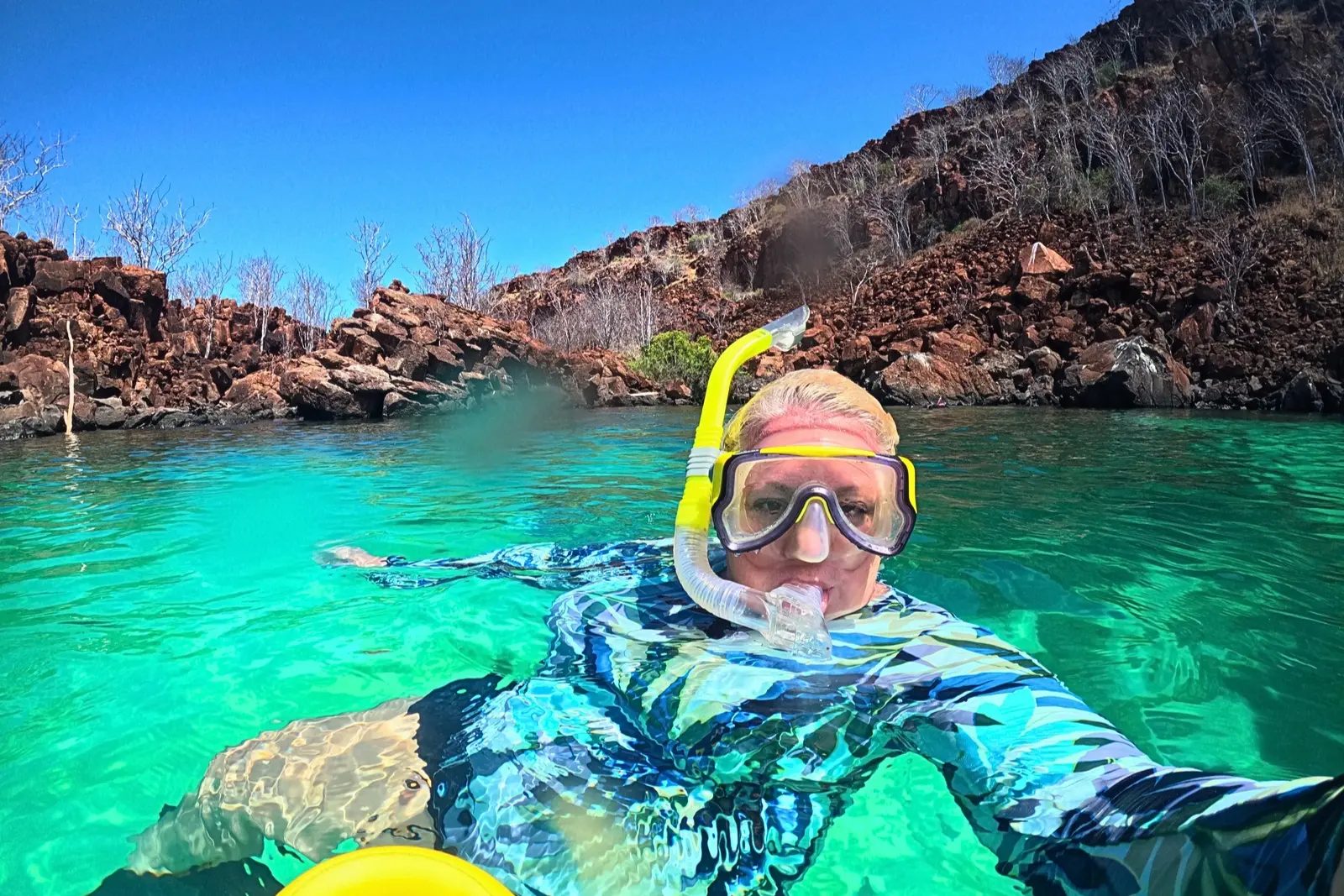 Erika Commisso snorkeling in turquoise water, with red rocky cliffs behind her.
