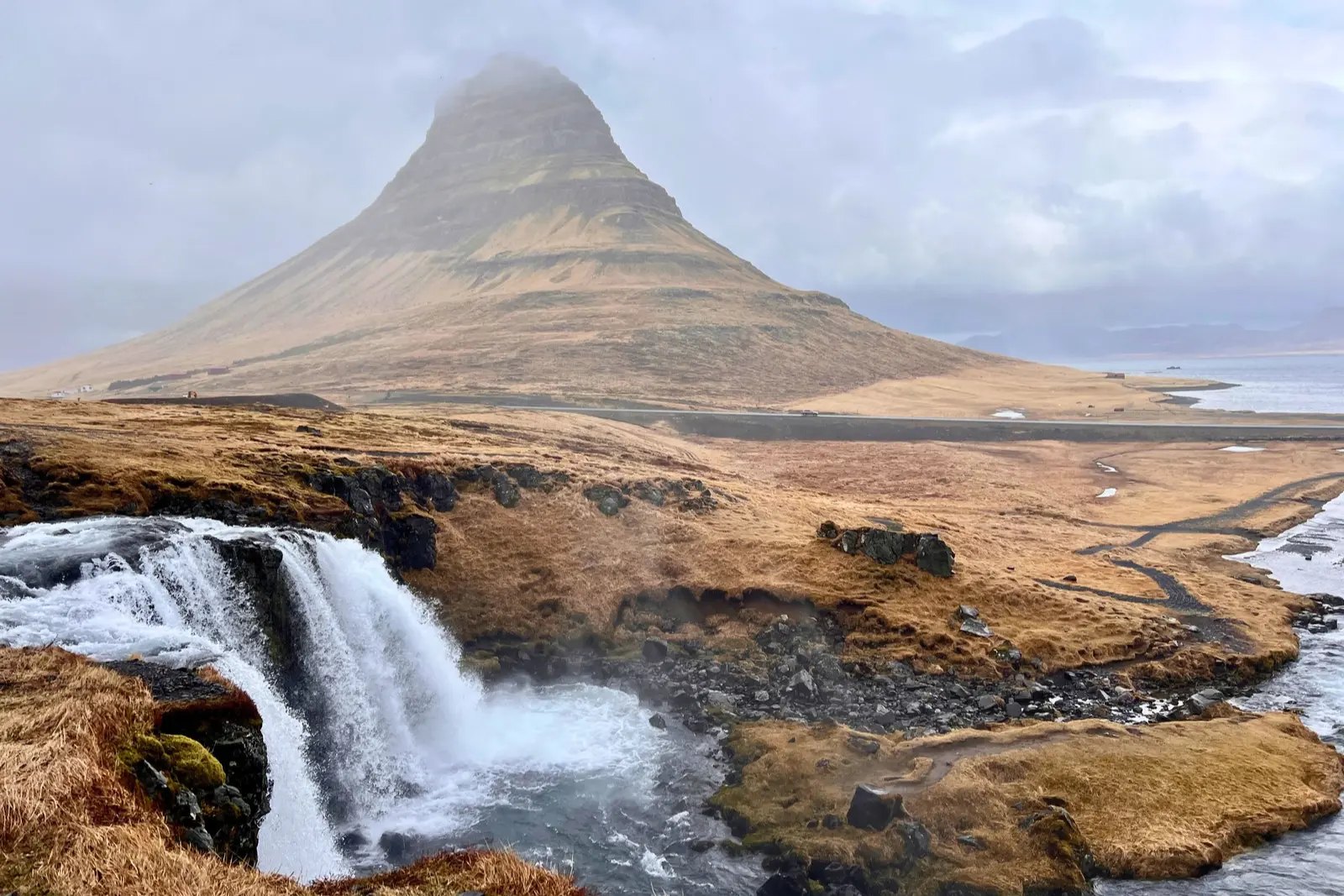 Kirkjufell's cone-shaped peak behind Kirkjufellsfoss, with golden winter grass.