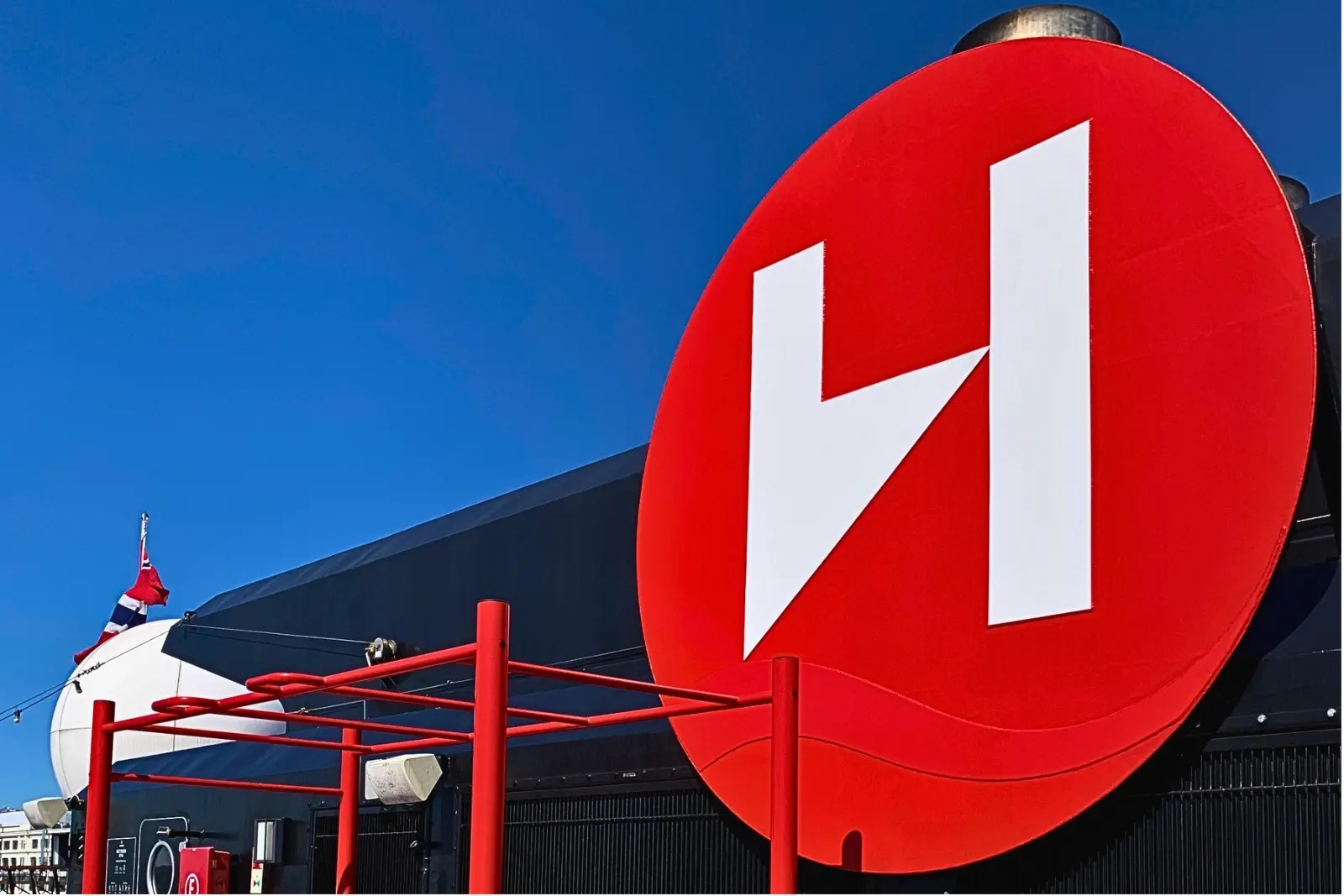 The Roald Amundsen's red funnel with a white H logo against a deep blue sky.