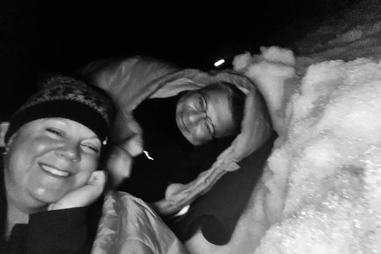 Chris and Erika Commisso lying in bivy bags dug into the snow at Eckener Point.
