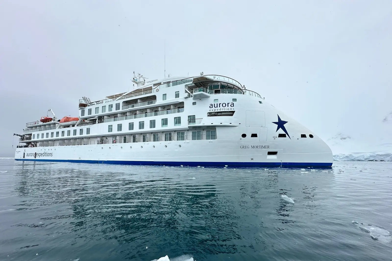 The Aurora Expeditions ship Greg Mortimer seen bow-on in calm water, with her inverted X-Bow and blue star on the hull.