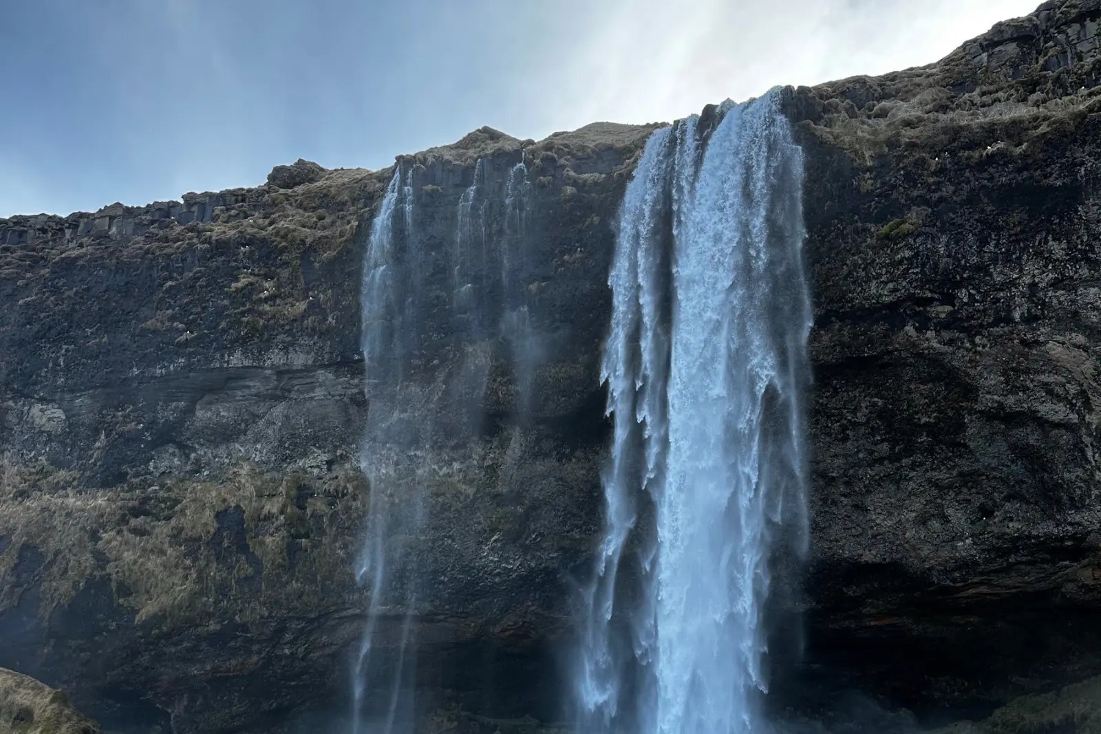 Seljalandsfoss falling from a mossy cliff under a blue sky.