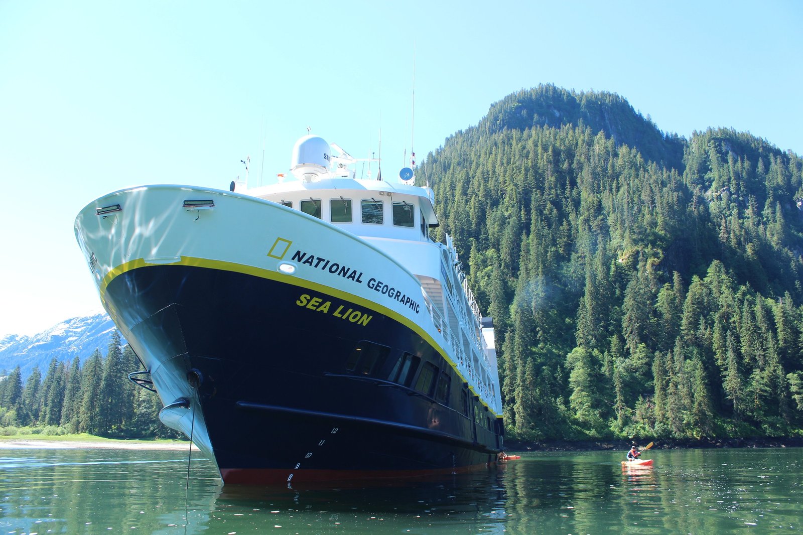The National Geographic Sea Lion anchored in a forested Alaskan cove with a kayaker alongside.