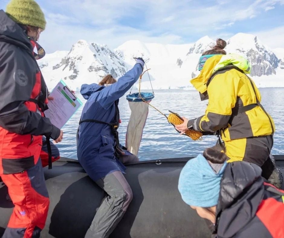 Researchers collecting water samples with a plankton net from a boat off Antarctica's snowy mountains