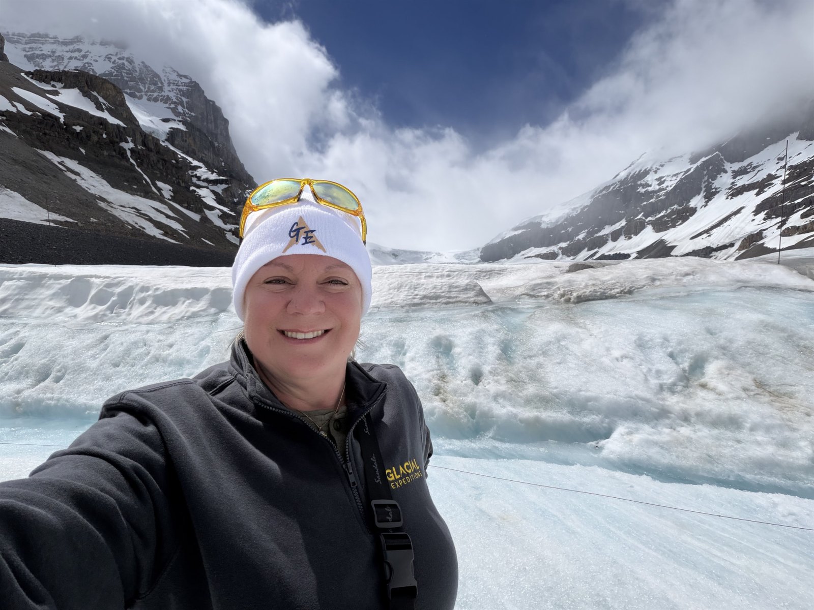 Erika Commisso in a Glacial Expeditions fleece and hat standing on a glacier ringed by snow-covered peaks.