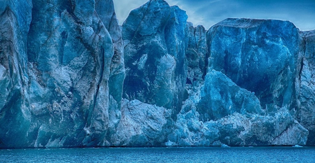 Green aurora borealis reflecting off the calm, iceberg-filled water of Scoresby Sund at night.