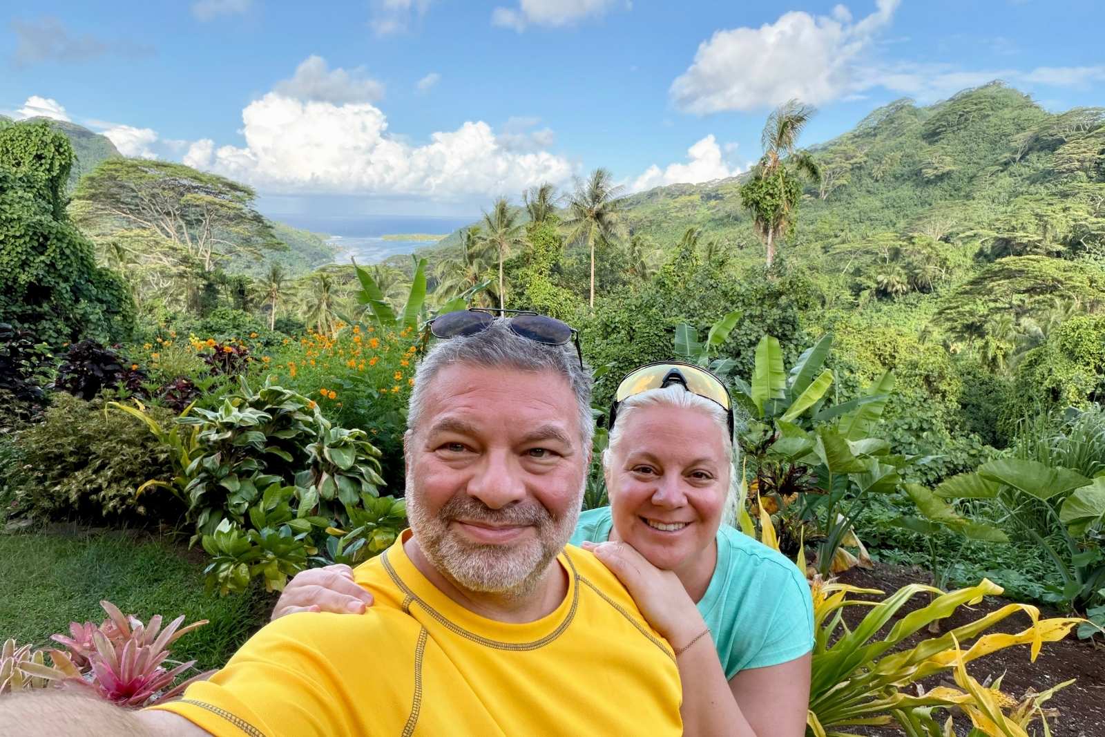 Chris and Erika Commisso at the Belvedere viewpoint on Huahine, with steep green mountains and the lagoon behind them.