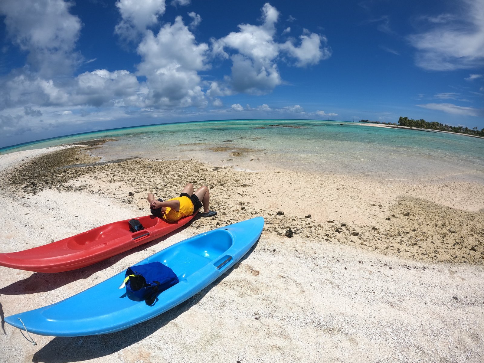 Two sit-on-top kayaks pulled up on a coral sandbar beside a shallow turquoise lagoon under scattered cloud.