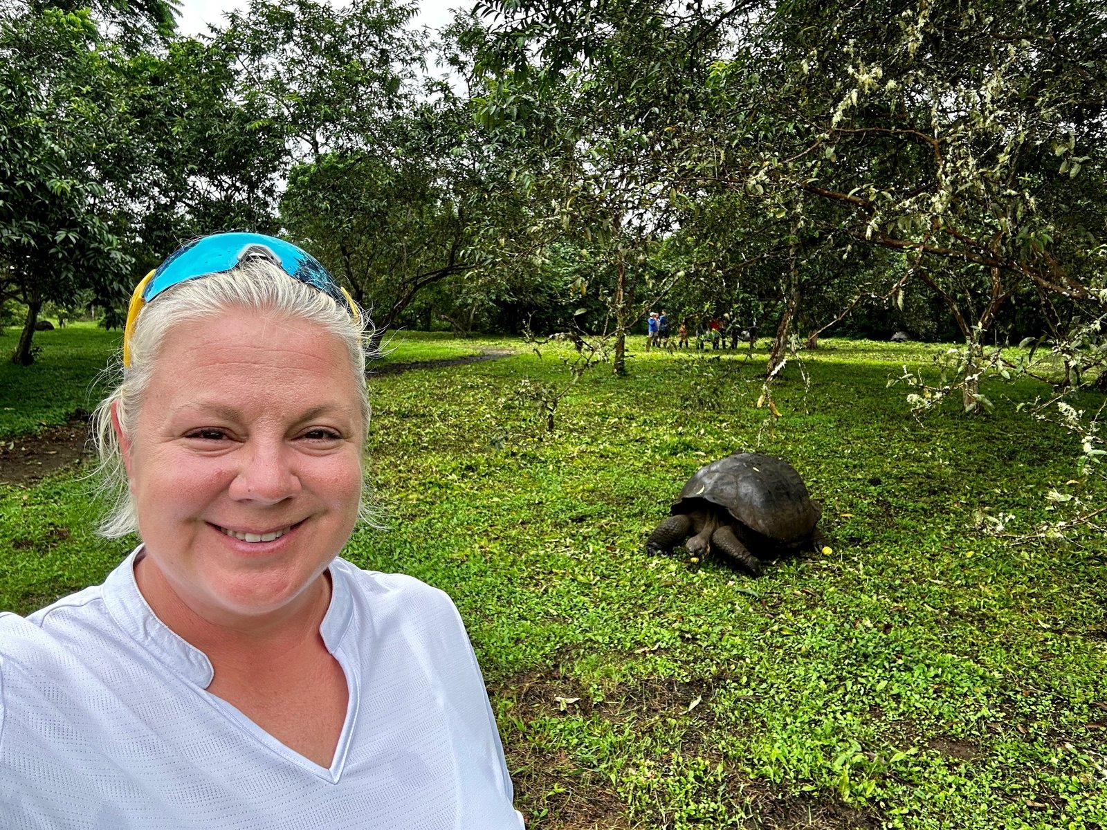 Erika Commisso smiling in the Galapagos highlands with a giant tortoise grazing on the grass behind her.