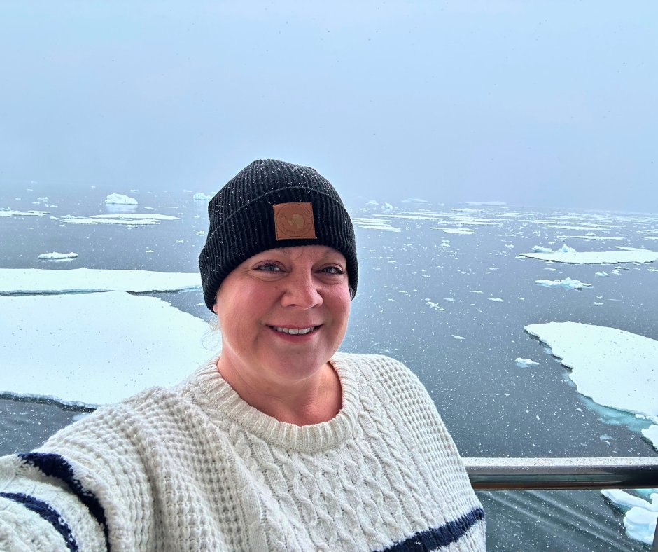 Erika Commisso in a knit beanie and cable-knit sweater on an Arctic voyage with icebergs behind her.