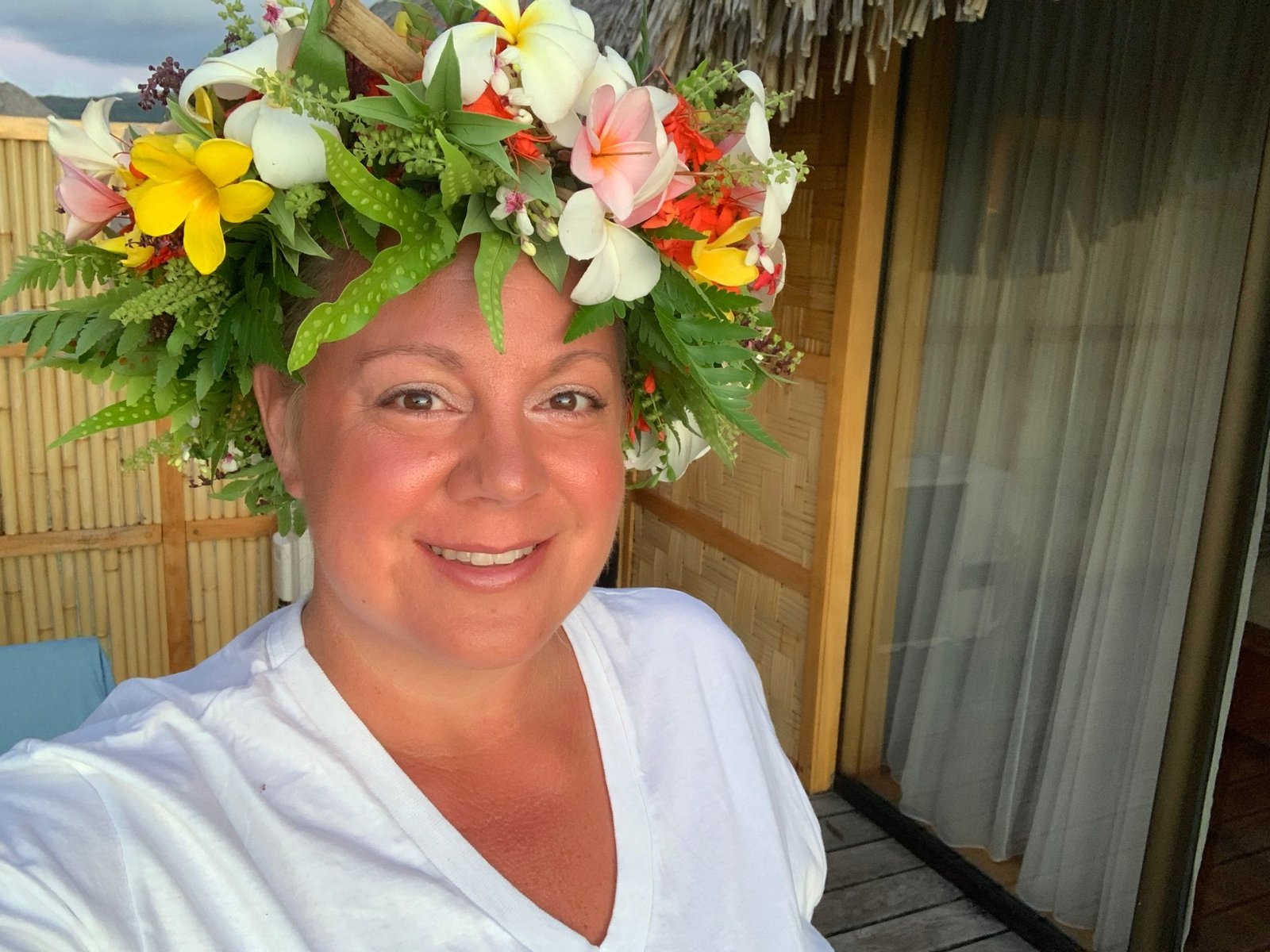 Erika Commisso wearing a fresh flower crown of frangipani, lilies and ferns on a bamboo-walled island terrace.