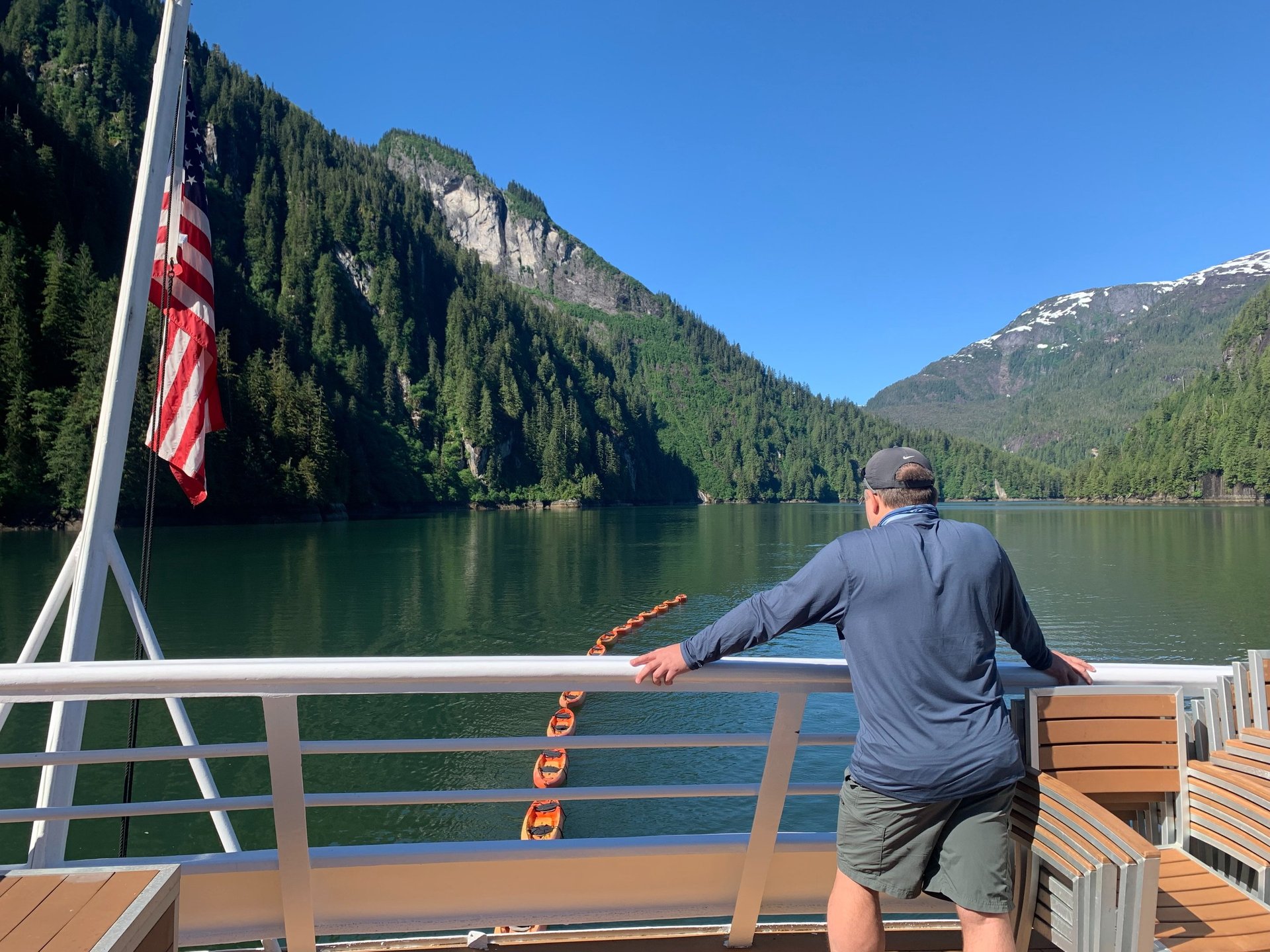 A passenger views the forested mountains of Misty Fjords National Monument from a tour boat deck.