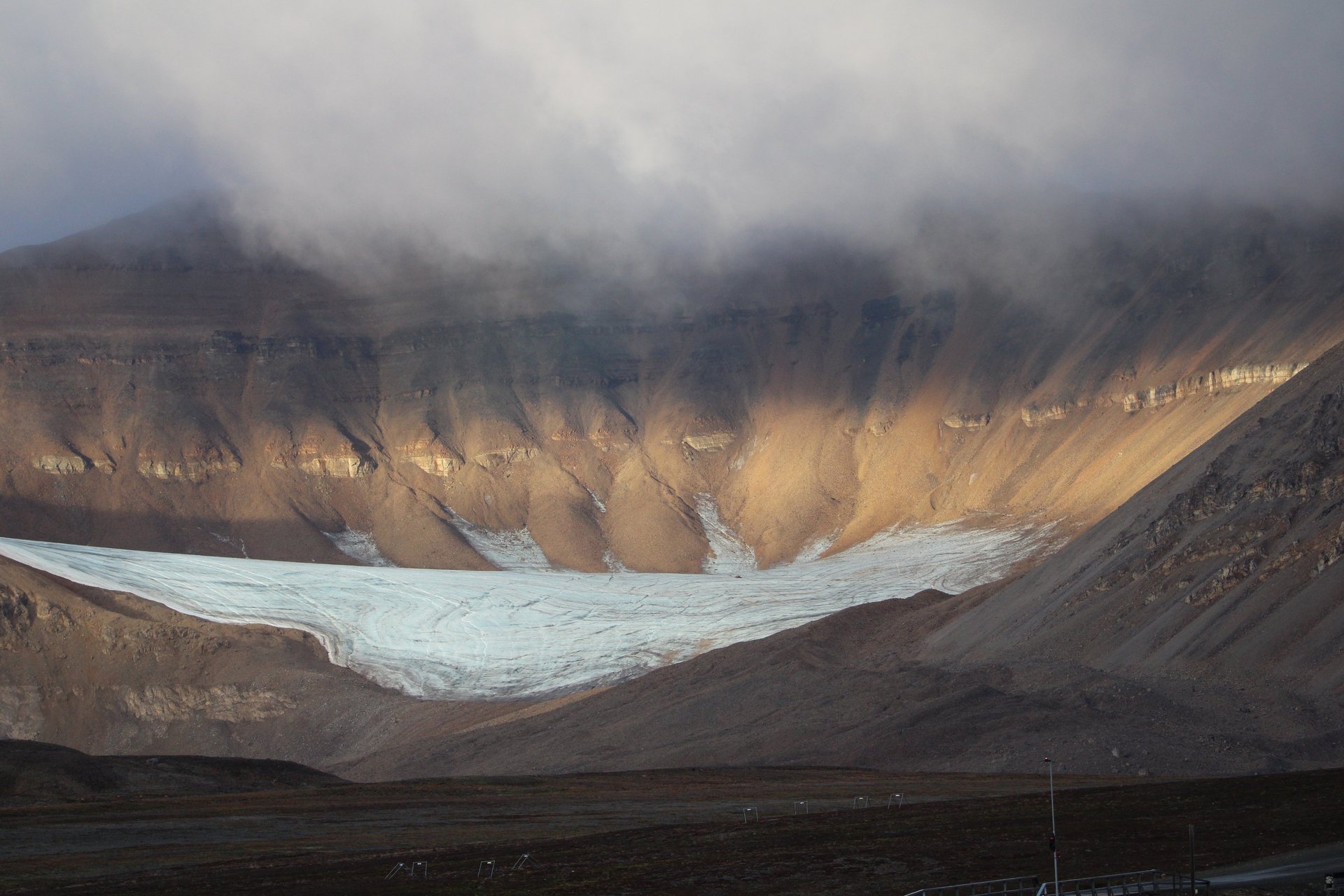 A glacier tongue spilling into a broad valley below cloud-covered brown cliffs near Longyearbyen.