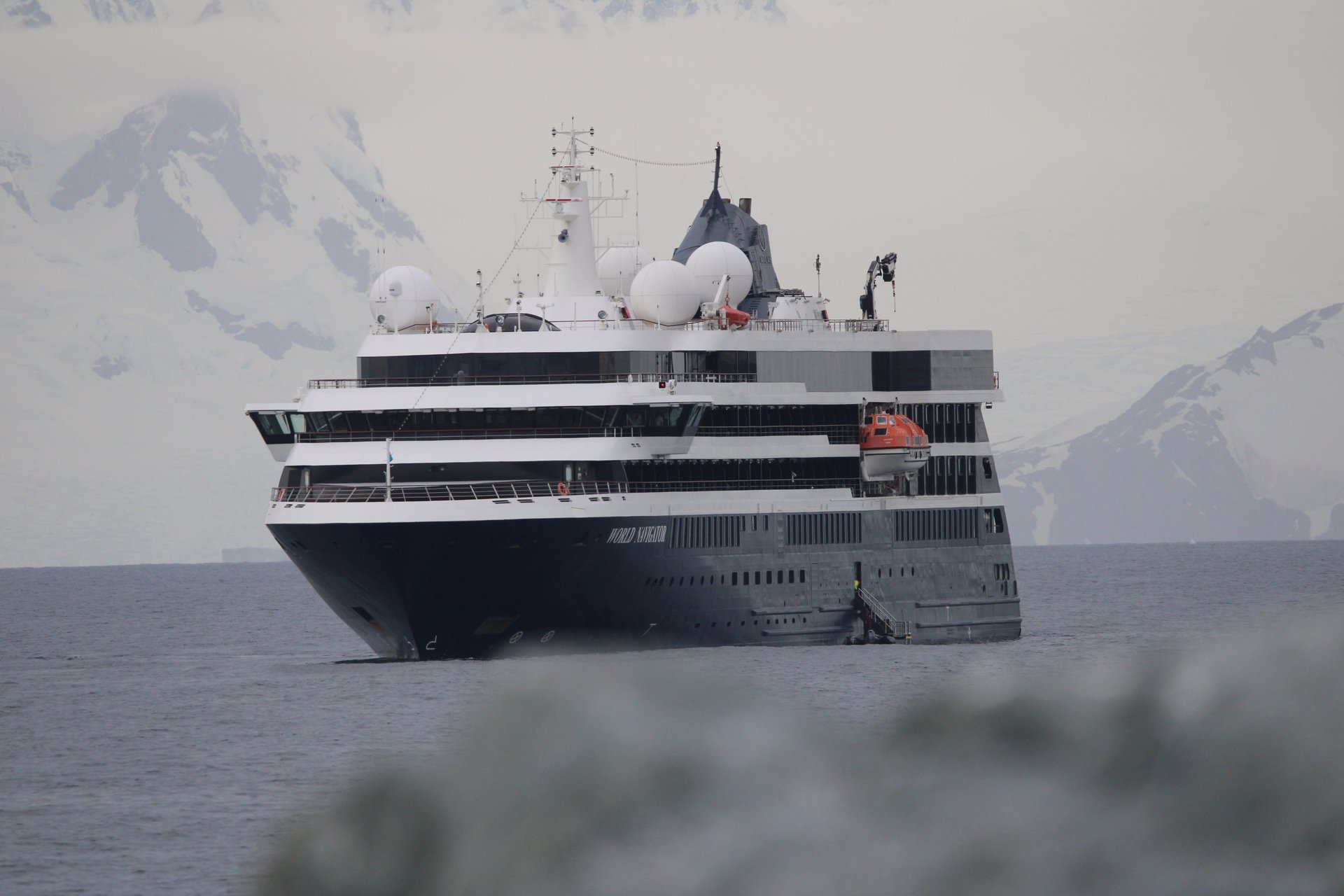 The expedition ship World Navigator at anchor in Antarctic water below snow-covered mountains.